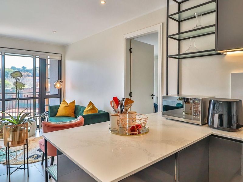 Modern open-plan apartment featuring a sleek kitchen with stone island, integrated shelving, and seamless flow to a private balcony with natural light.