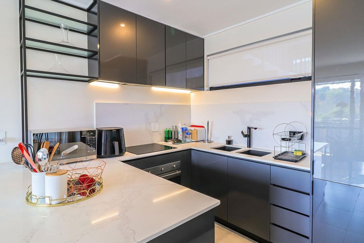 A modern, well-appointed kitchen featuring sleek dark cabinetry, quartz countertops, integrated appliances, and stylish under-cabinet lighting.