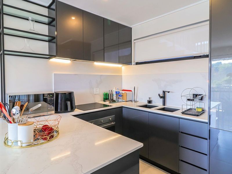 A modern, well-appointed kitchen featuring sleek dark cabinetry, quartz countertops, integrated appliances, and stylish under-cabinet lighting.
