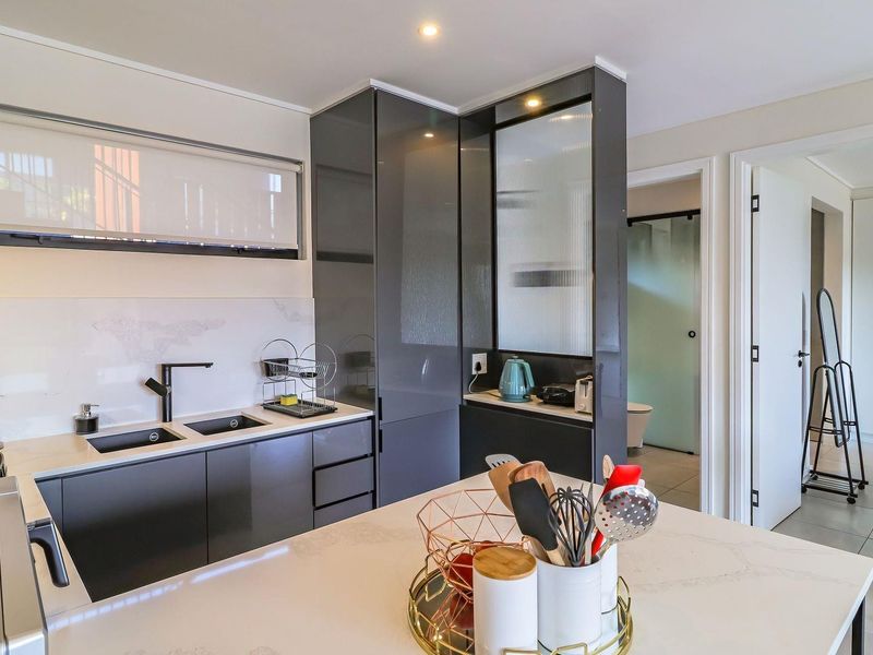 Modern kitchen featuring sleek dark cabinetry, quartz countertops, a double undermount sink, and high-quality finishes with an adjacent view into the bathroom area.