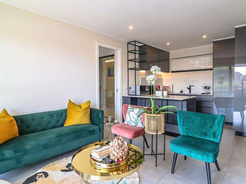 Modern open-plan living area featuring a sleek, contemporary kitchen with dark cabinetry, a central island, and high-quality tiled flooring throughout.
