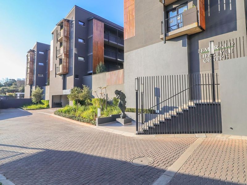 Exterior view of the modern apartment complex entrance, featuring paved driveway, secure metal fencing, and contemporary architectural facade details.