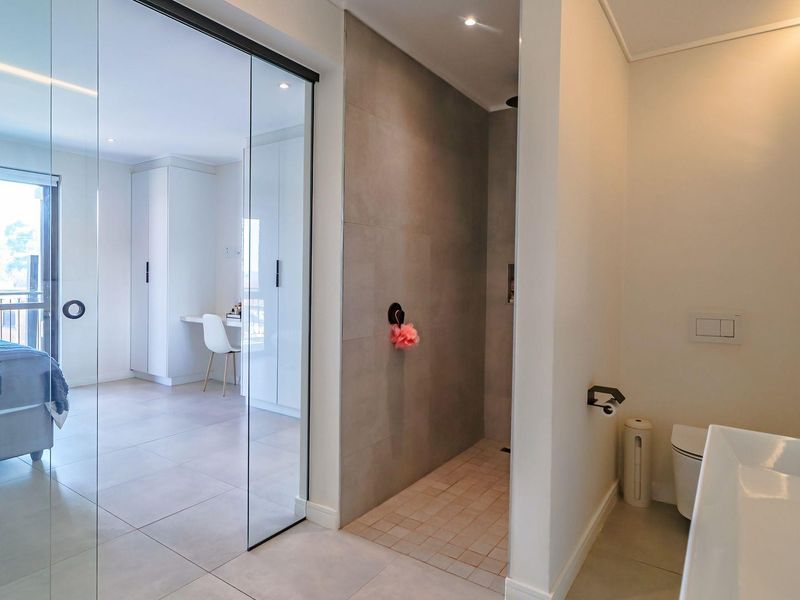 Modern en-suite bathroom featuring a walk-in shower, wall-mounted toilet, and sleek vanity, seamlessly integrated with the adjacent bedroom through a glass partition.