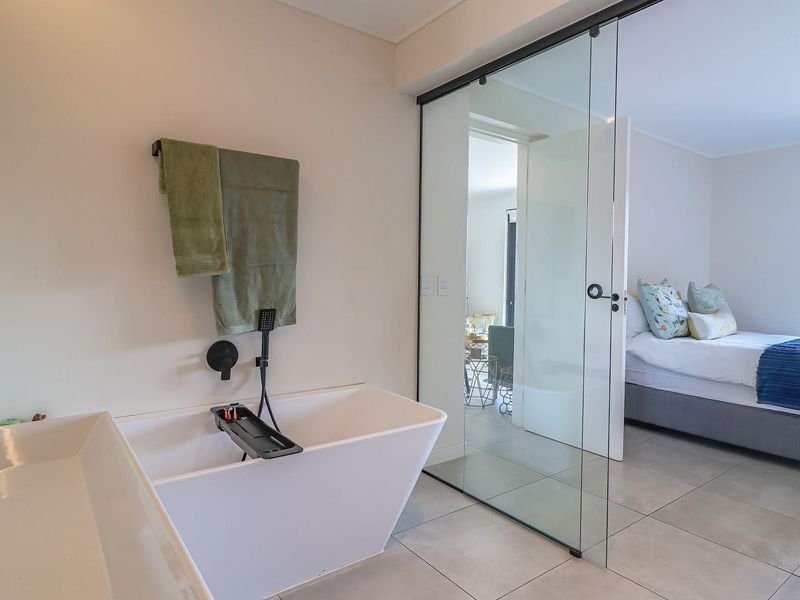 Modern en-suite bathroom featuring a sleek freestanding bathtub, wall-mounted fixtures, and a contemporary glass partition wall separating the space from the bedroom.