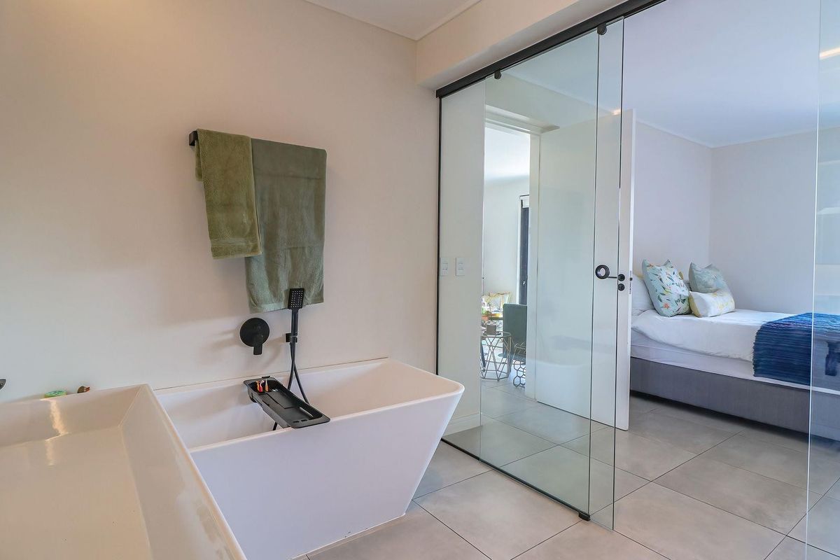 Modern en-suite bathroom featuring a sleek freestanding bathtub, wall-mounted fixtures, and a contemporary glass partition wall separating the space from the bedroom.