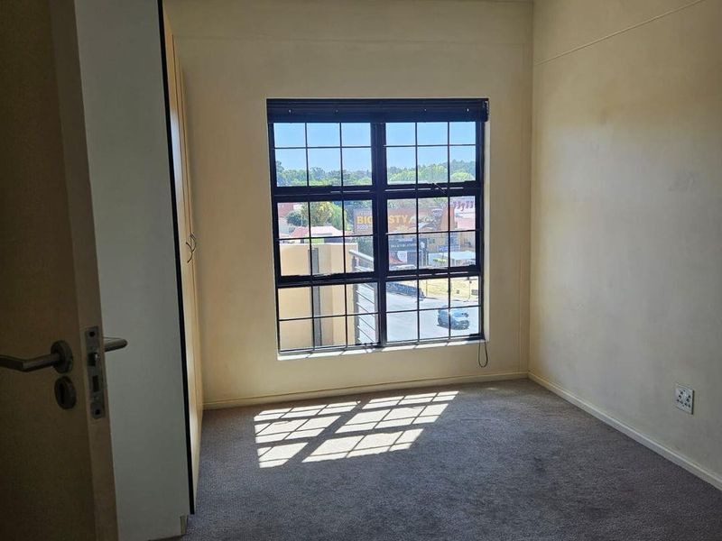 A vacant bedroom featuring a built-in wardrobe, carpeted flooring, and a grid-pattern window with natural light.