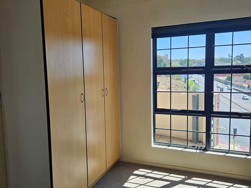 A bright, empty bedroom featuring a built-in wooden wardrobe and a large grid-pattern window with views of the surrounding area.