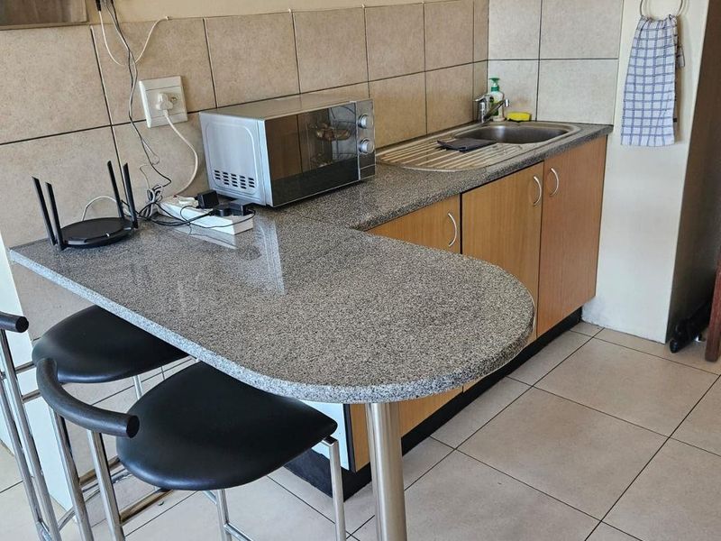 Compact kitchen area featuring granite countertops, a stainless steel sink, tiled backsplash, and functional built-in cabinetry with a breakfast bar extension.