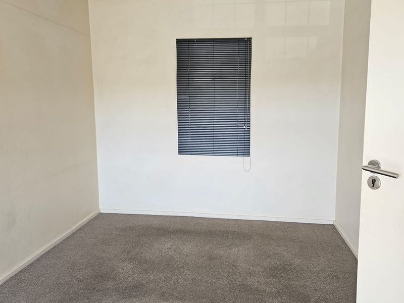 An empty bedroom featuring neutral walls, carpet flooring, and a window fitted with venetian blinds.