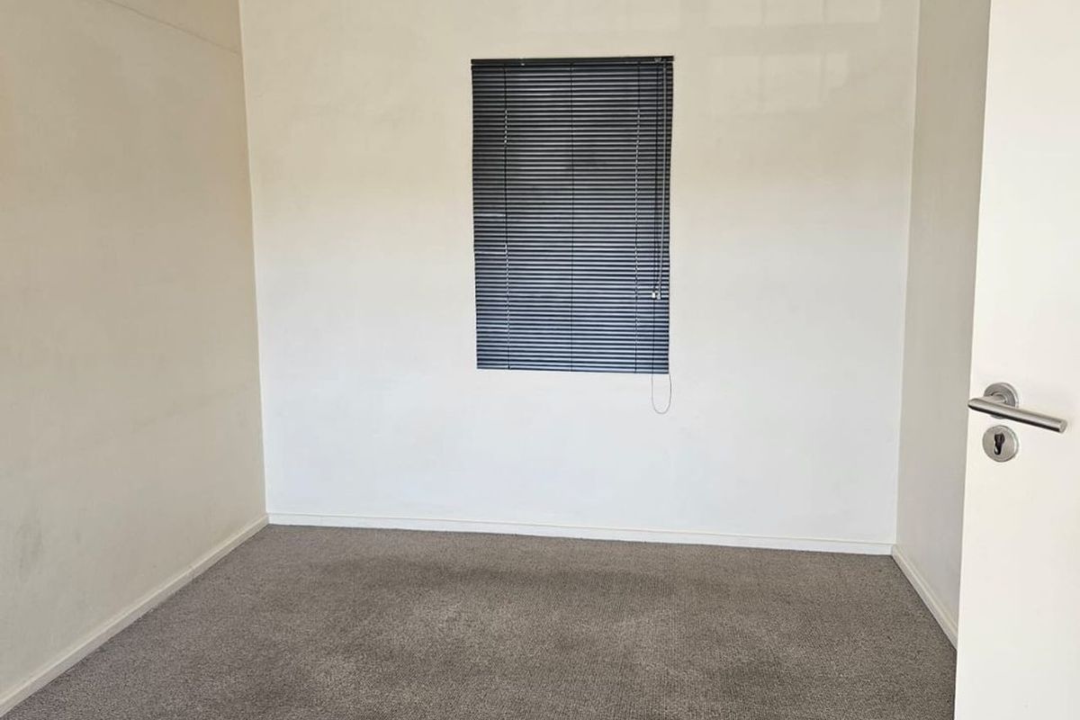 An empty bedroom featuring neutral walls, carpet flooring, and a window fitted with venetian blinds.