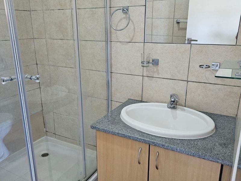 A functional bathroom featuring a glass shower enclosure, a vanity cabinet with a granite countertop, and a wall-mounted mirror.