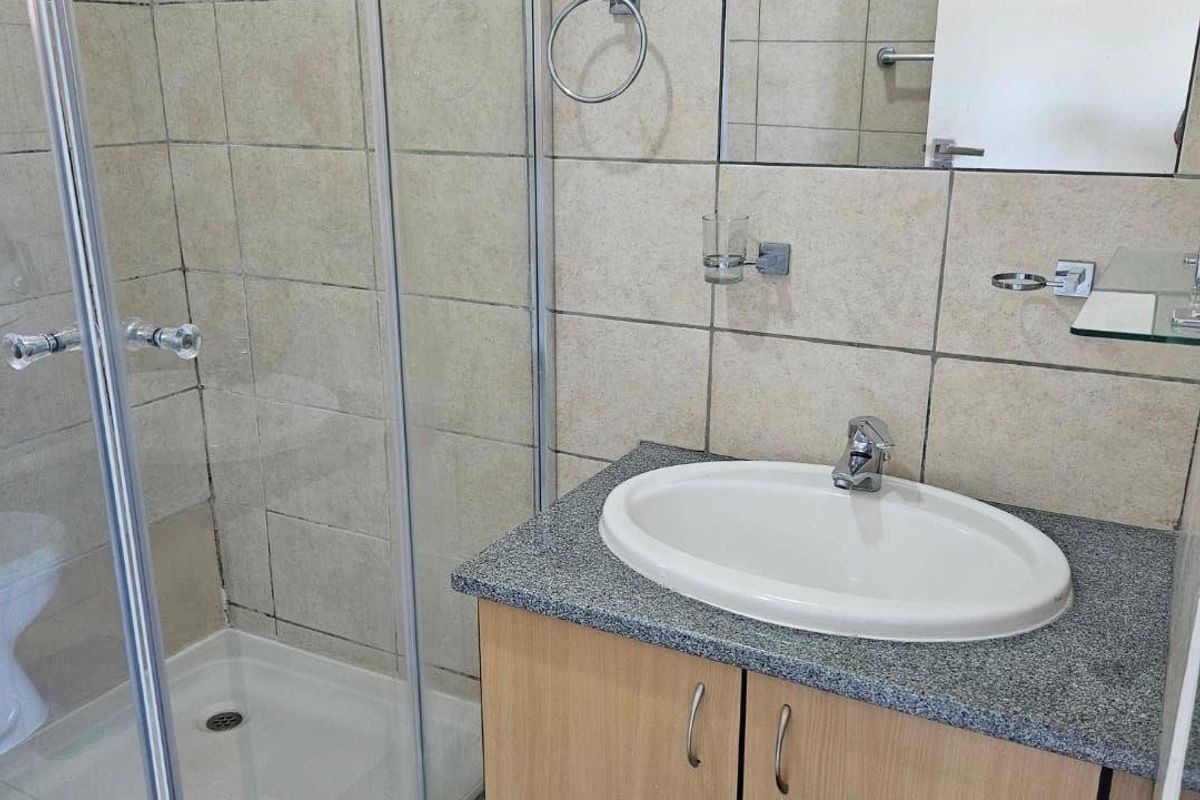 A functional bathroom featuring a glass shower enclosure, a vanity cabinet with a granite countertop, and a wall-mounted mirror.