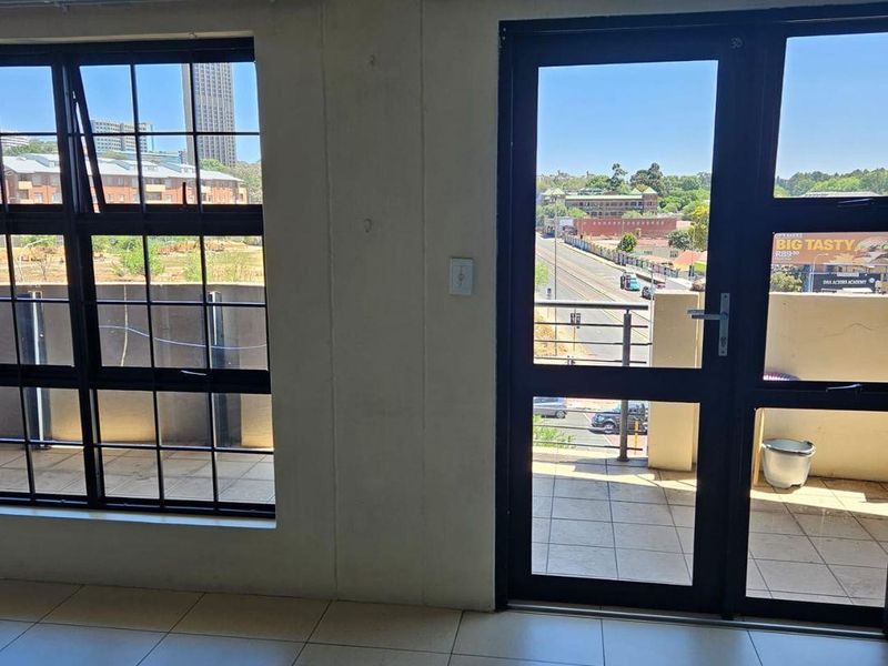 An empty living area featuring tiled flooring and large black aluminium windows and a door leading out to a balcony with urban views.