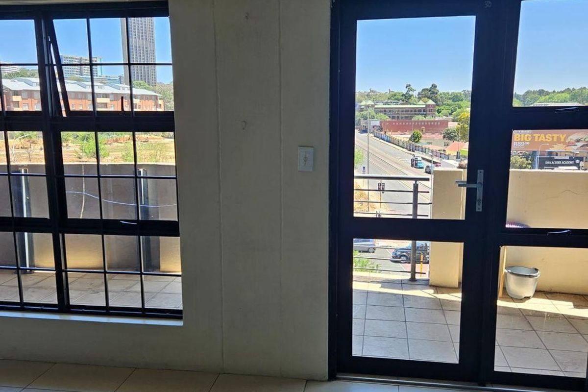 An empty living area featuring tiled flooring and large black aluminium windows and a door leading out to a balcony with urban views.