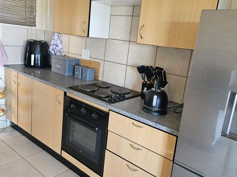 A functional kitchen featuring light wood-finish cabinetry, granite countertops, a tiled backsplash, and built-in electric cooking appliances.