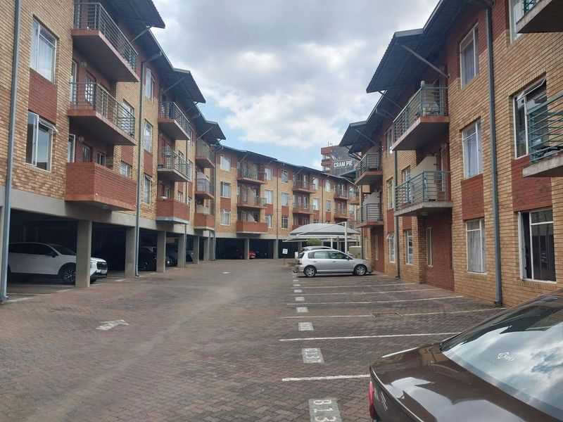 Exterior view of a multi-story apartment complex featuring brick facades, private balconies, and an open-air paved parking area for residents.