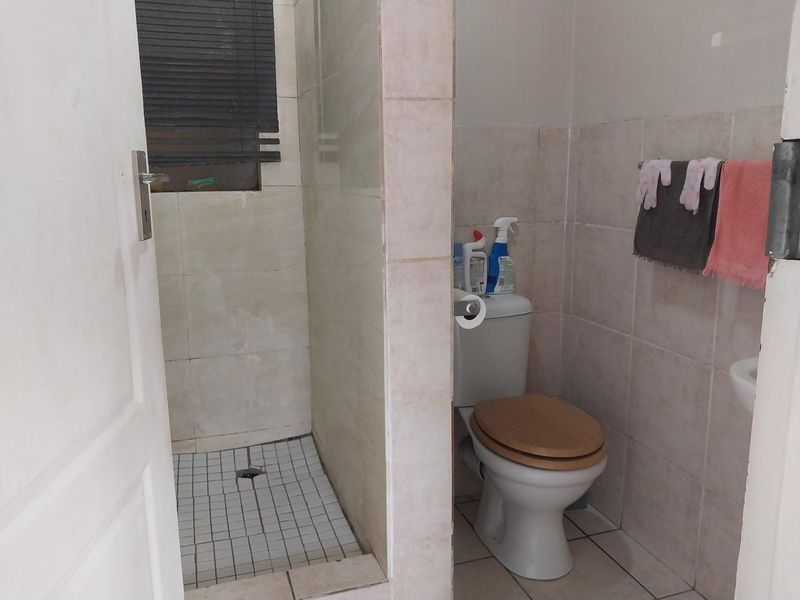 A functional bathroom featuring a tiled shower enclosure, toilet, and neutral wall tiling, offering a practical layout with potential for cosmetic updates.