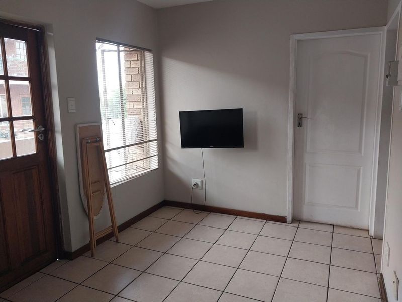 A simple, tiled living area featuring a timber-framed glass door, venetian blinds, and a wall-mounted television point.