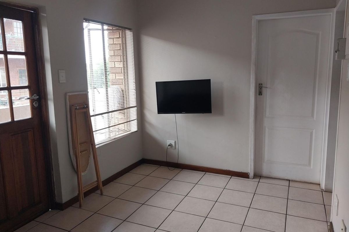 A simple, tiled living area featuring a timber-framed glass door, venetian blinds, and a wall-mounted television point.