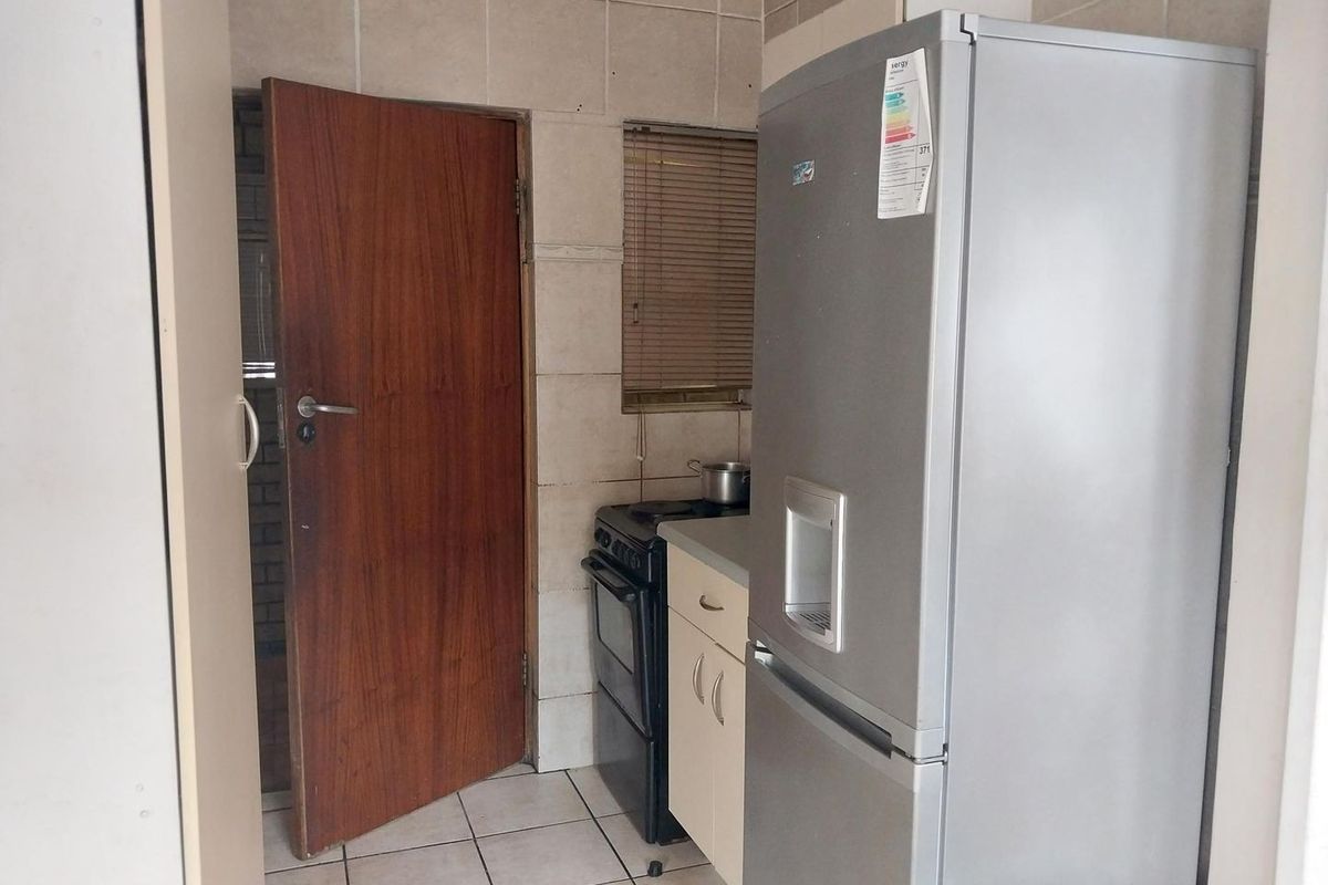 A compact kitchen area featuring tiled flooring, wall splashbacks, and built-in cabinetry, providing a functional space that could benefit from modern updates.