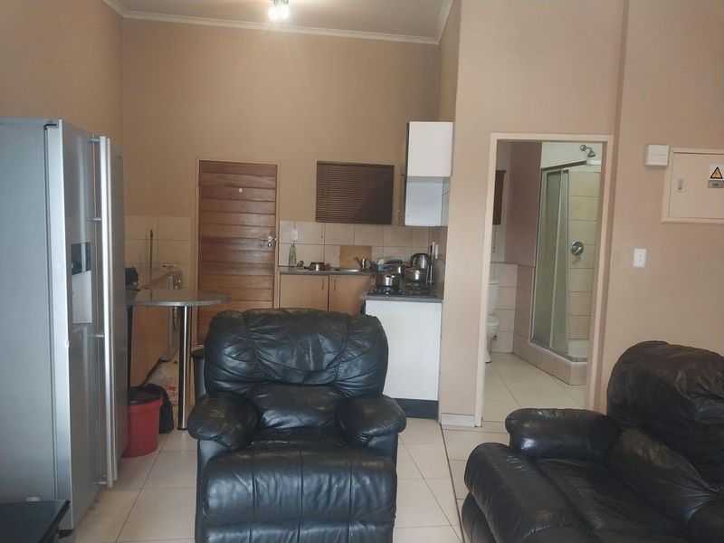 Open plan living area featuring a compact kitchen with cabinetry and an adjacent bathroom with a shower enclosure and tiled finishes.