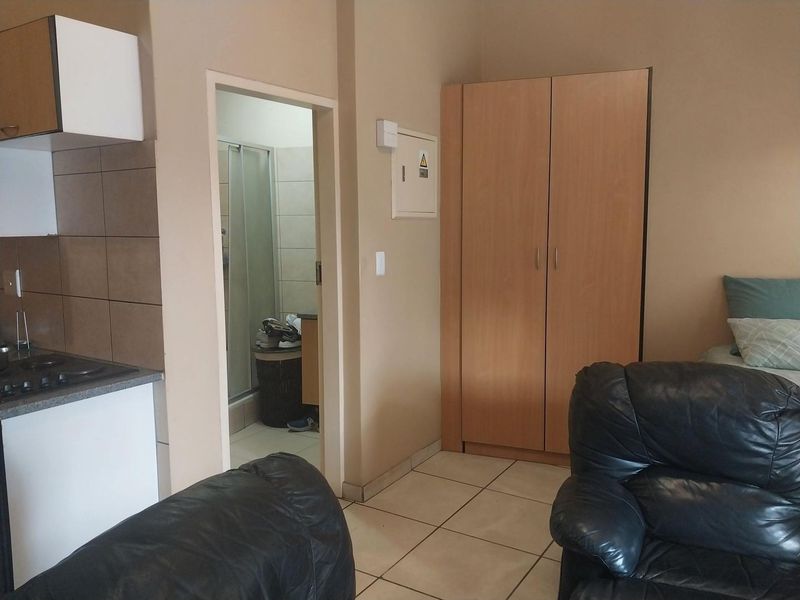 Open-plan living area featuring tiled flooring, built-in wardrobe, and a compact kitchen corner with hob, leading to an adjacent bathroom.