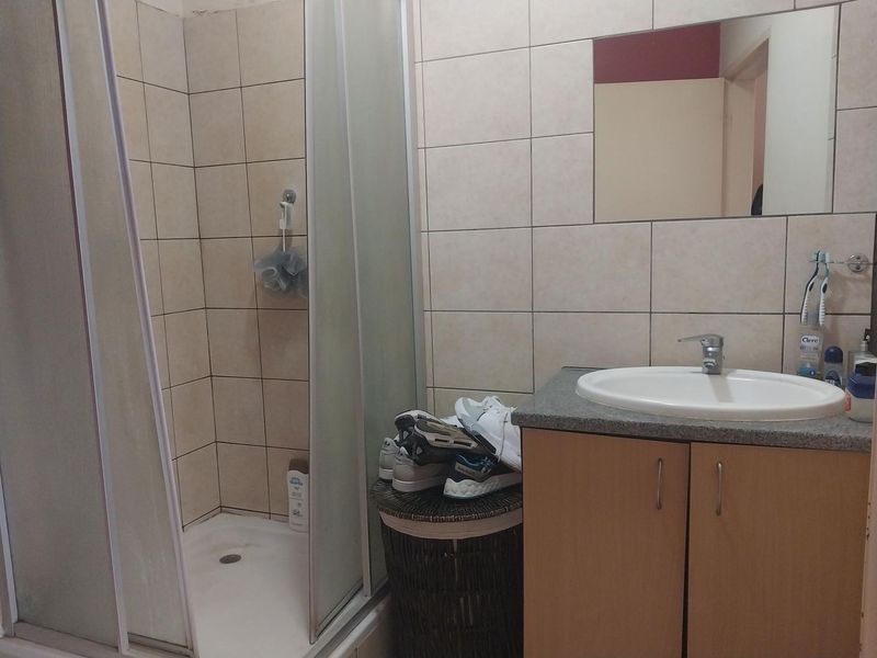 A functional bathroom featuring a shower enclosure, a vanity cabinet with a basin, and wall-mounted mirror with neutral tiled finishes.