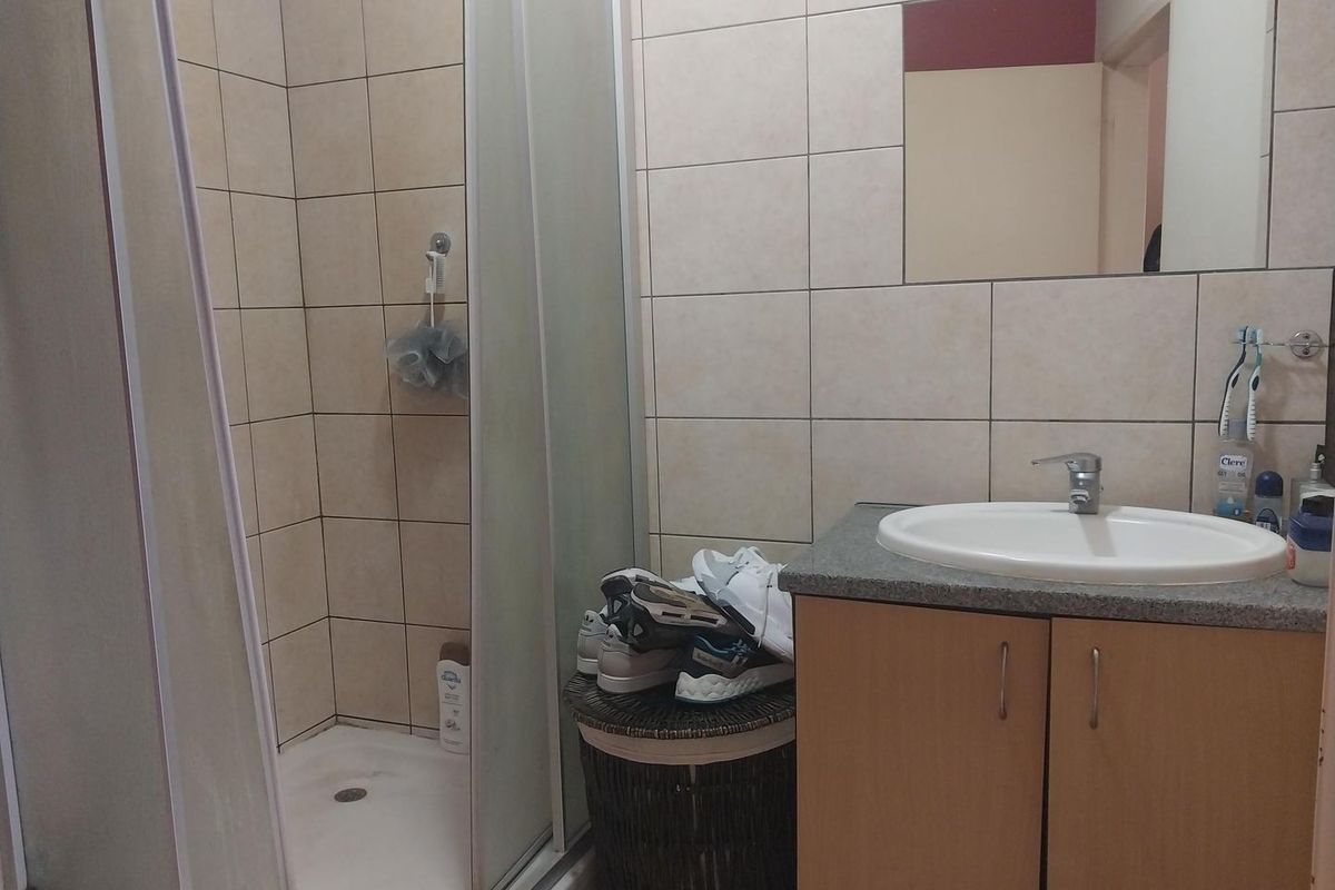 A functional bathroom featuring a shower enclosure, a vanity cabinet with a basin, and wall-mounted mirror with neutral tiled finishes.