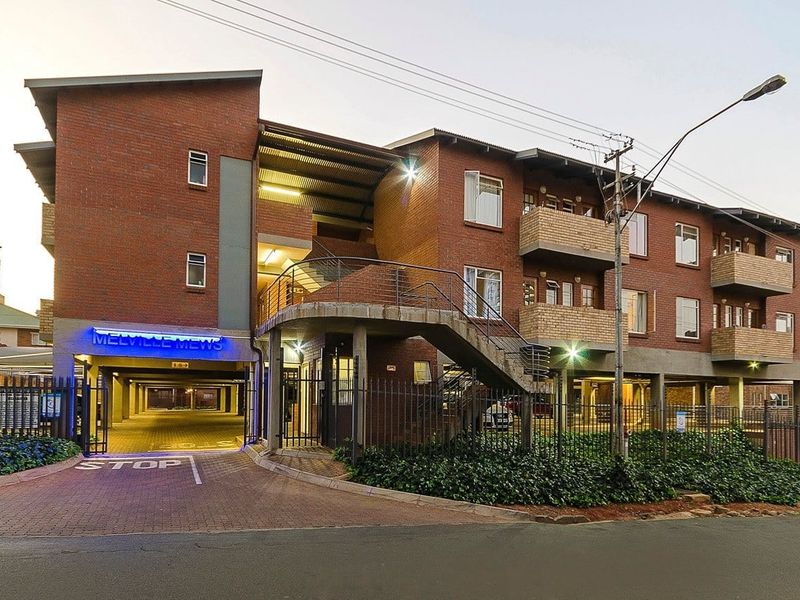 Front elevation of Melville Mews apartment complex featuring brick facade, undercover parking access, external staircases, and private balconies.