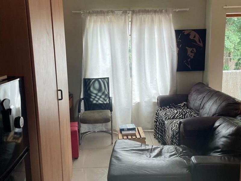 A living room area featuring tiled flooring and a built-in cupboard, with access to a balcony through a windowed door.