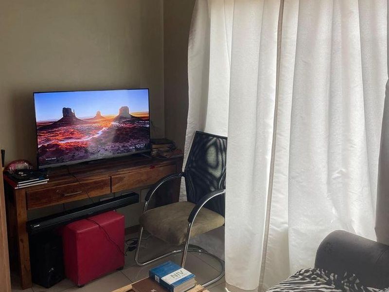 A compact living area featuring tiled flooring and natural light through window curtains, suitable for a cozy lounge or home office setup.