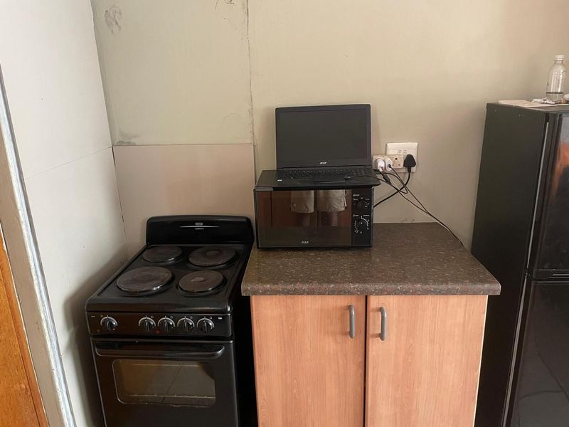 A compact kitchen area featuring a freestanding stove, laminate countertop, and base cabinetry, showing signs of wear on the surrounding wall surfaces.