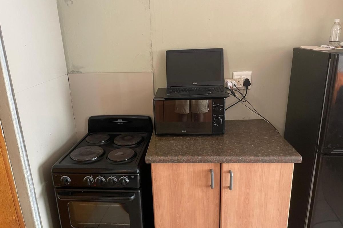 A compact kitchen area featuring a freestanding stove, laminate countertop, and base cabinetry, showing signs of wear on the surrounding wall surfaces.