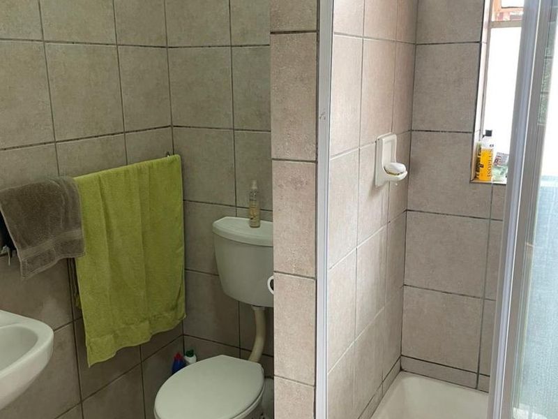 A functional bathroom featuring a shower enclosure, toilet, and pedestal basin with neutral ceramic tiling throughout.