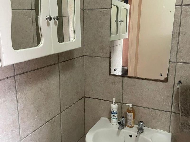 A compact bathroom featuring a wall-mounted basin, tiled walls, and a medicine cabinet, showing signs of wear and dated finishes.