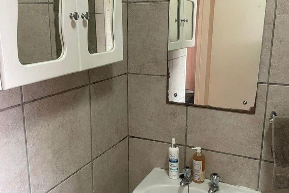 A compact bathroom featuring a wall-mounted basin, tiled walls, and a medicine cabinet, showing signs of wear and dated finishes.