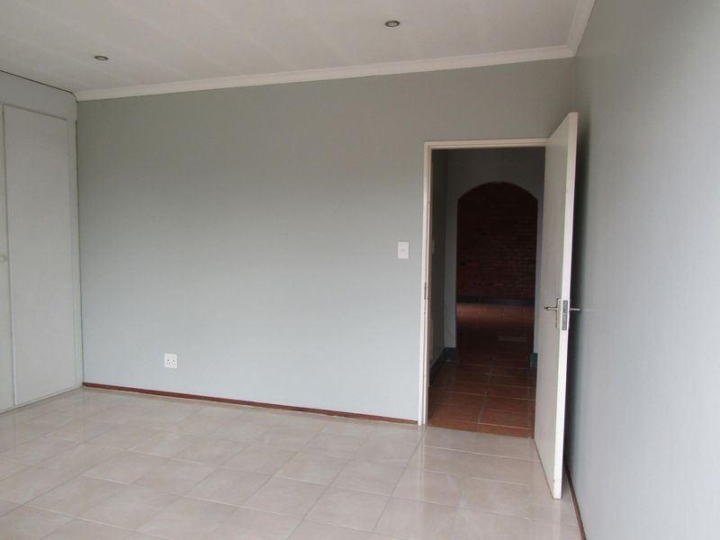 An empty bedroom featuring neutral grey walls, tiled flooring, and built-in cupboard storage with recessed ceiling lighting.