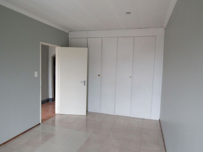 An empty bedroom featuring built-in cupboards, neutral grey walls, and tiled flooring, offering a blank canvas for personalization.