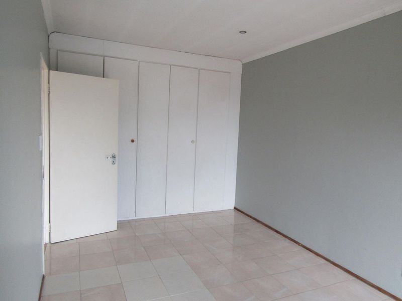 A clean, empty bedroom featuring neutral grey walls, tiled flooring, and ample built-in cupboard storage.