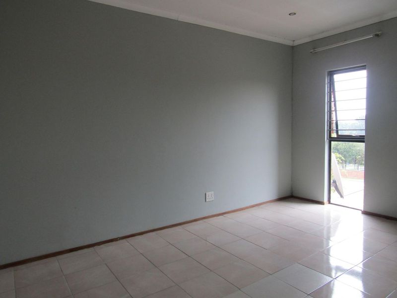 An empty bedroom featuring neutral grey walls, tiled flooring, and a window with security bars, offering a clean canvas for personalization.
