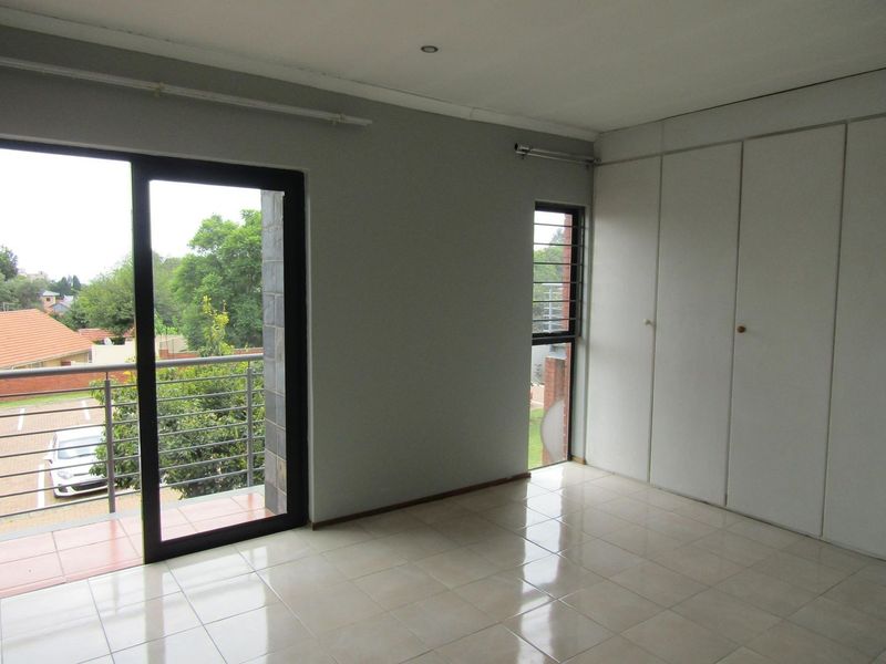 A bright, empty bedroom featuring tiled flooring, built-in cupboards, and a sliding glass door providing access to a private balcony.
