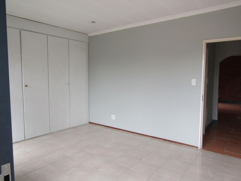 A clean, empty bedroom featuring neutral grey walls, tiled flooring, and built-in cupboards, offering a versatile space ready for personalization.