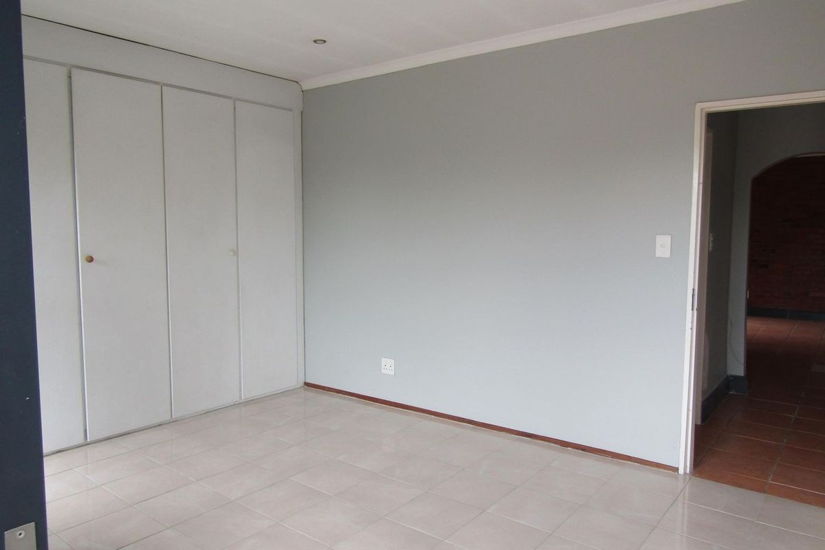 A clean, empty bedroom featuring neutral grey walls, tiled flooring, and built-in cupboards, offering a versatile space ready for personalization.