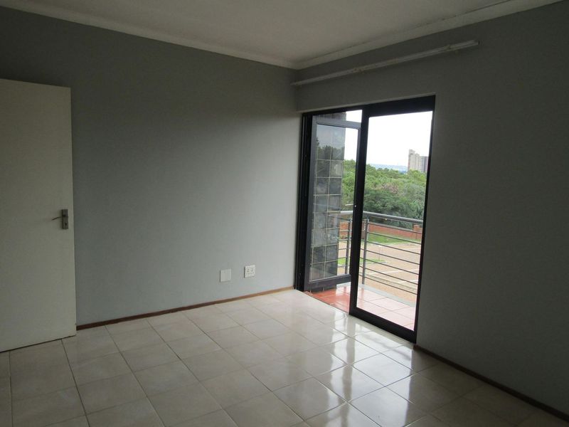 An empty bedroom featuring tiled flooring and a sliding glass door that provides direct access to a private balcony.
