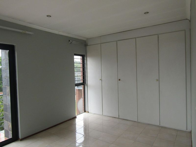 An empty bedroom featuring tiled flooring, built-in cupboards, recessed lighting, and a sliding glass door providing access to an outdoor area.