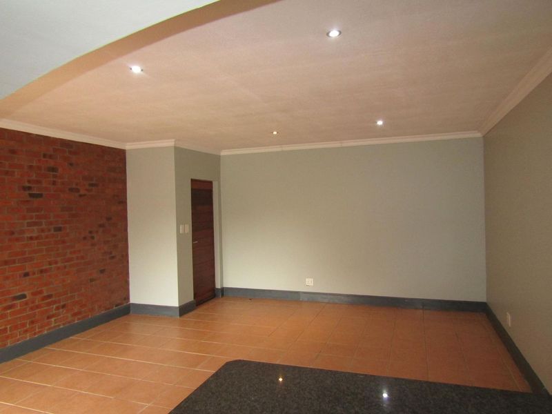 Spacious living area featuring an exposed brick accent wall, neutral painted walls, tiled flooring, and modern recessed downlighting.