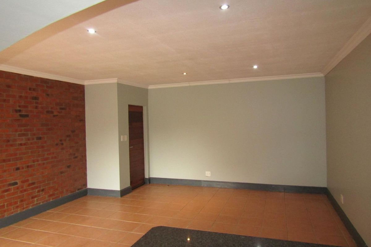 Spacious living area featuring an exposed brick accent wall, neutral painted walls, tiled flooring, and modern recessed downlighting.