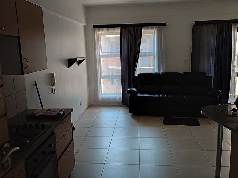 Open-plan living area featuring tiled flooring and a functional kitchen with built-in cabinetry, oven, and hob, leading to a bright lounge space.