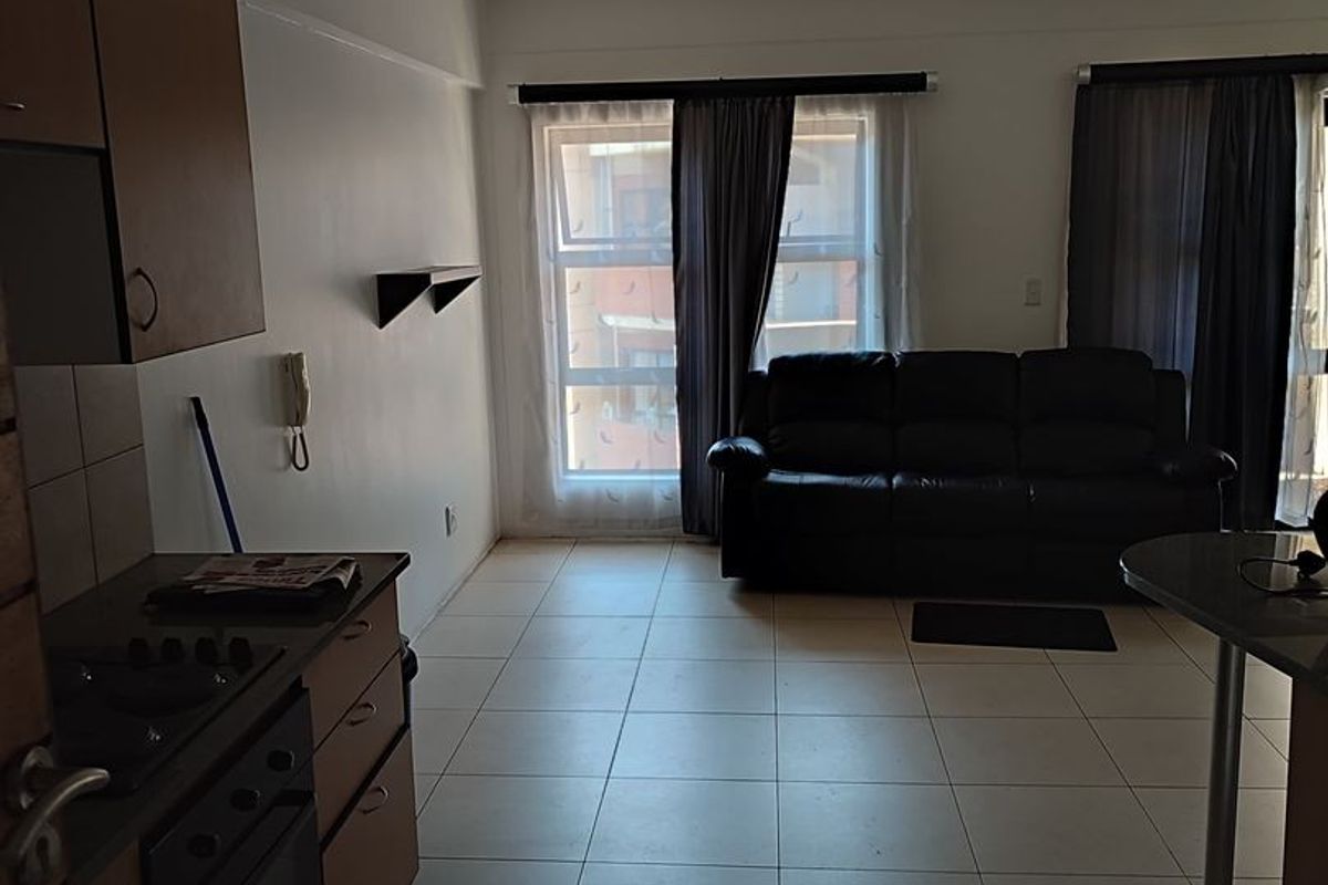 Open-plan living area featuring tiled flooring and a functional kitchen with built-in cabinetry, oven, and hob, leading to a bright lounge space.