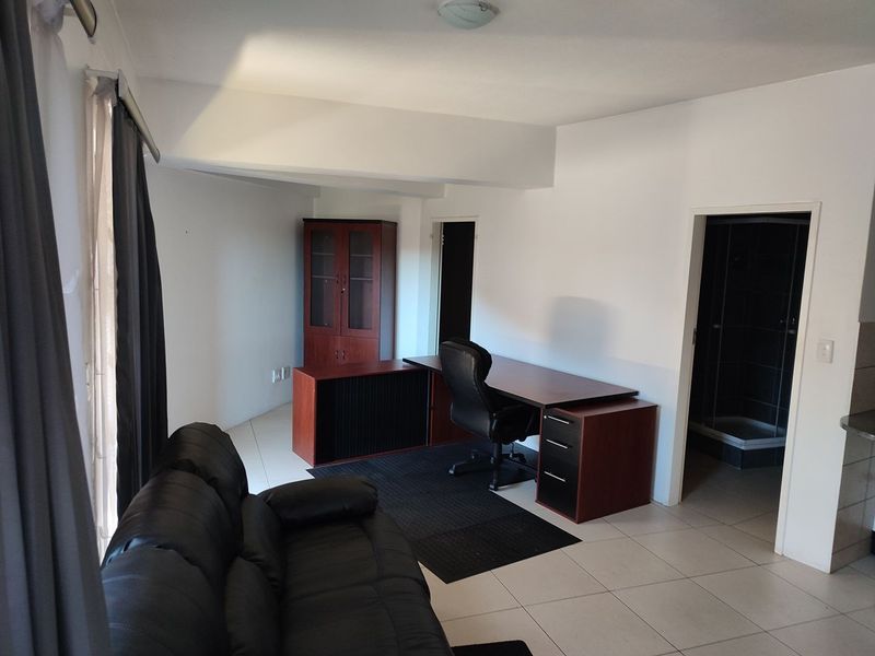A functional office space featuring neutral tiled flooring and direct access to an adjacent bathroom area.